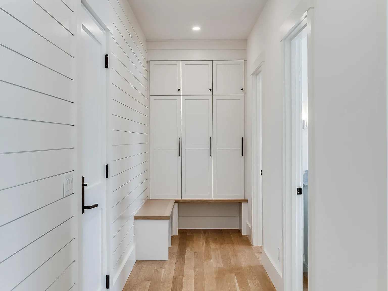 Mudroom — shiplap walls, custom white cabinetry, built-in bench, black hardware
